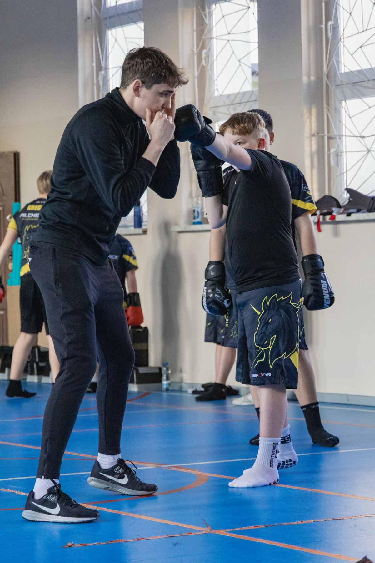 Trener i uczeń ćwiczą, chłopiec wyprowadza cios w kierunku trenera